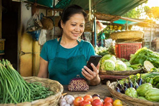 A produce vendor checking her phone beside market baskets